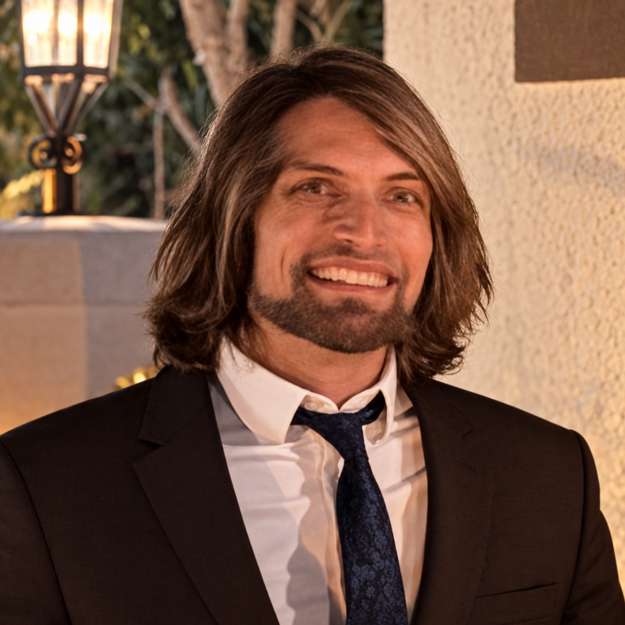 Joshua Handrich smiling in a dark suit, white shirt, and blue tie