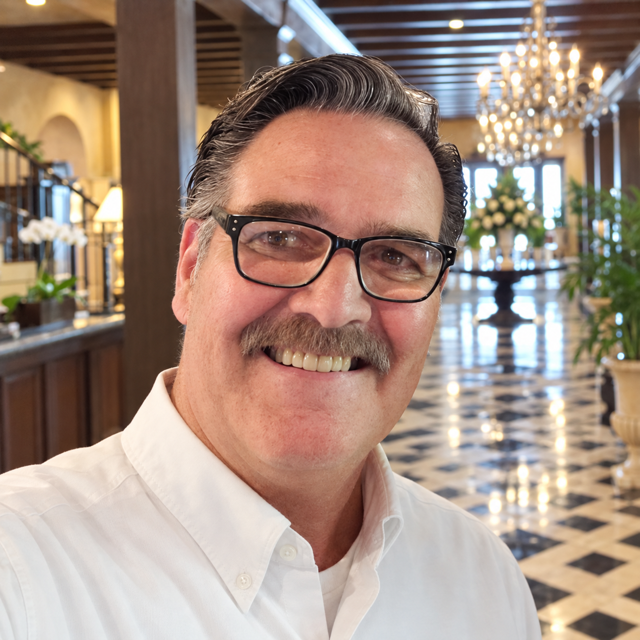 Russell Betts smiling in a white shirt and glasses