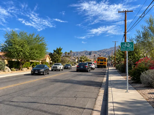 Supplied West Drive artwork showing a school bus, traffic, a sidewalk, a bike-route sign, and mountains.